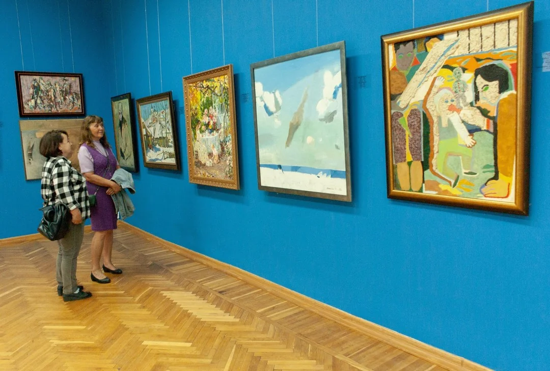 Дві жінки розглядають картини на синій стіні художньої галереї