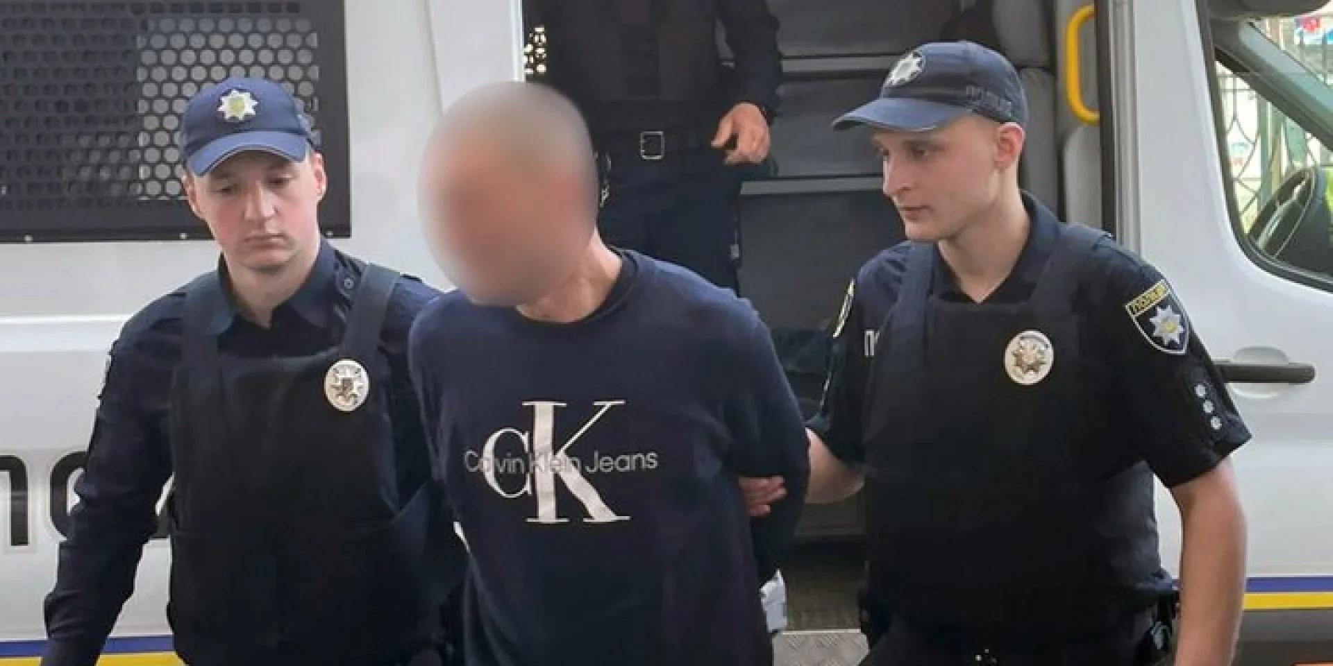 Поліцейські конвоюють затриманого у Львові чоловіка біля спецавтомобіля