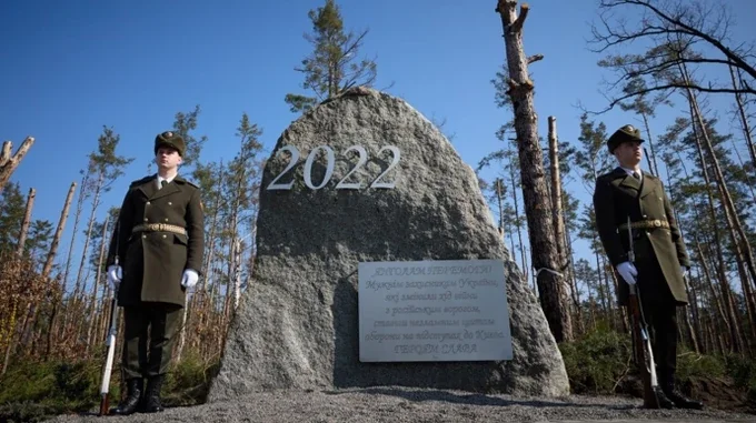 Два військові біля гранітного пам’ятника 2022 року з дошкою на братській могилі вояків УНР