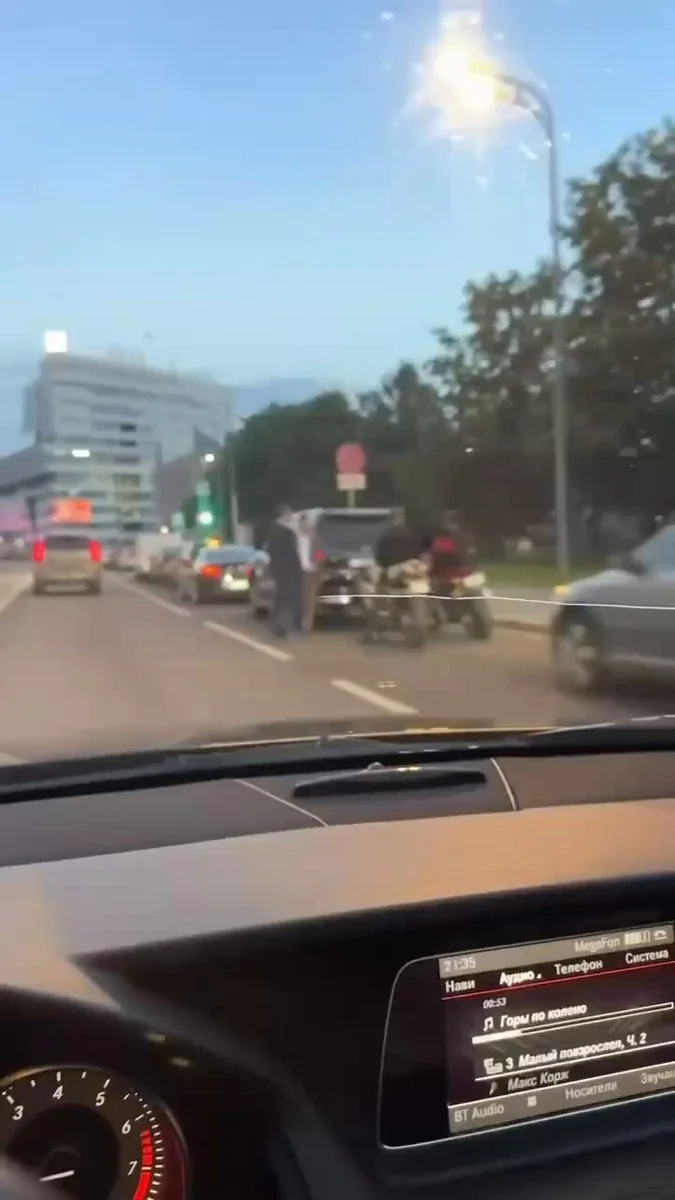 Вид з салону авто на вечірню міську дорогу з машинами та людьми біля зупиненого транспорту