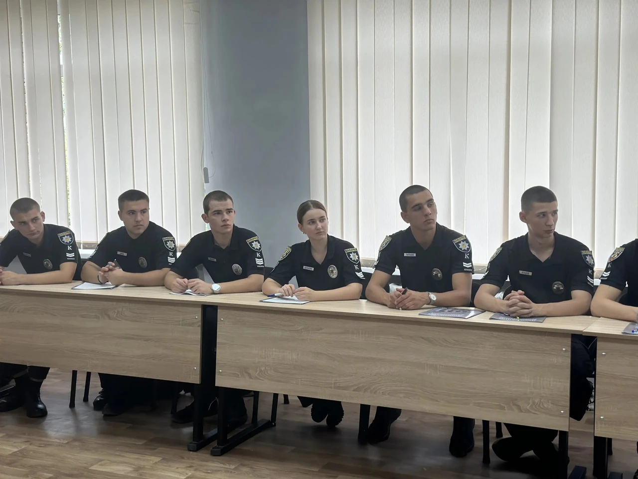 Посадовці та представники правоохоронних органів стоять разом у офіційному приміщенні